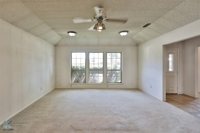 empty room featuring light colored carpet, vaulted ceiling, a textured ceiling, and ceiling fan