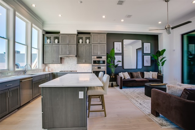 kitchen featuring a center island, light hardwood / wood-style flooring, appliances with stainless steel finishes, ceiling fan, and a breakfast bar