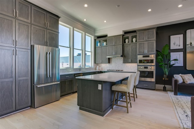 kitchen featuring a breakfast bar, crown molding, light wood-type flooring, appliances with stainless steel finishes, and a kitchen island