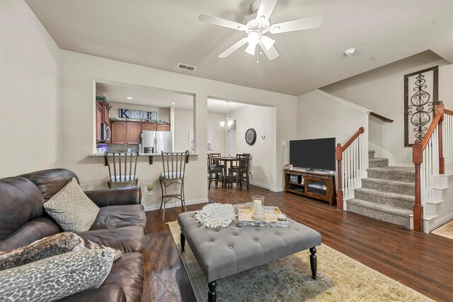 living room featuring ceiling fan with notable chandelier and dark wood-type flooring