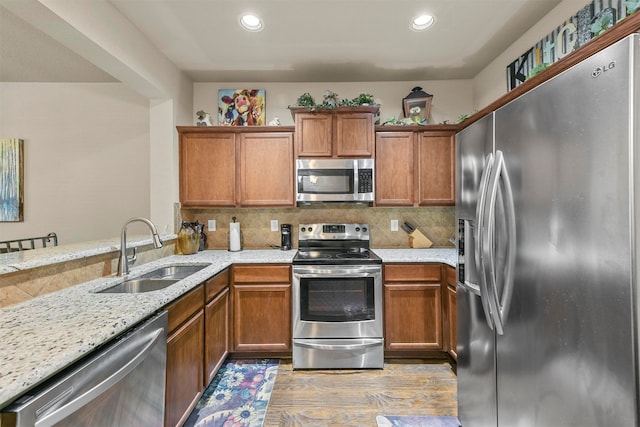 kitchen with light wood-type flooring, light stone counters, sink, decorative backsplash, and appliances with stainless steel finishes