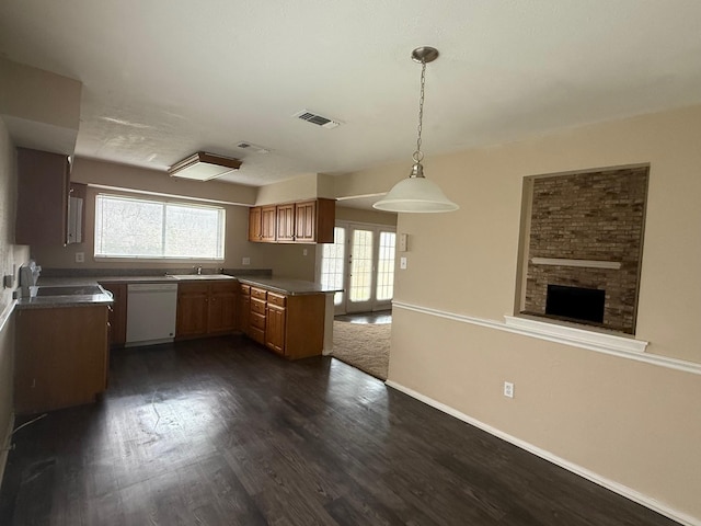 kitchen featuring white dishwasher, sink, hanging light fixtures, a fireplace, and dark hardwood / wood-style flooring