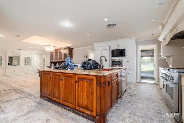 kitchen with high end range, oven, hanging light fixtures, an island with sink, and a notable chandelier