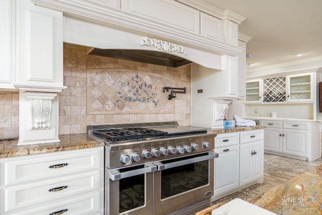 kitchen with custom exhaust hood, double oven range, backsplash, light stone countertops, and white cabinetry