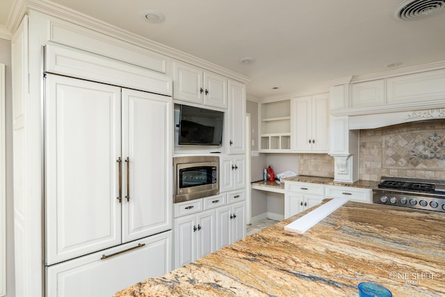 kitchen featuring decorative backsplash, light stone counters, crown molding, built in appliances, and white cabinets