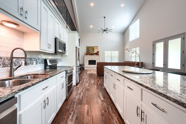 kitchen with dark wood-type flooring, stainless steel appliances, sink, white cabinets, and ceiling fan