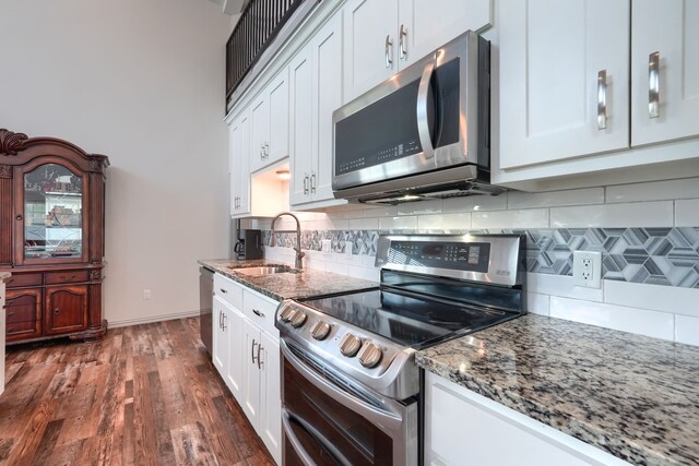 kitchen featuring white cabinets, appliances with stainless steel finishes, stone countertops, dark wood-type flooring, and sink