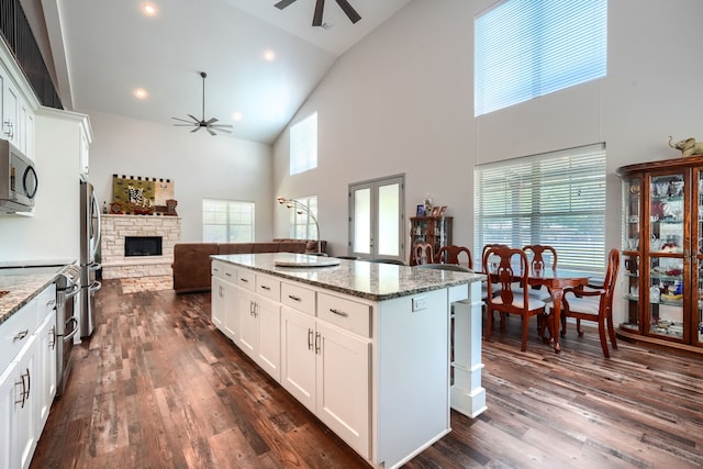 kitchen with a kitchen island, white cabinetry, light stone counters, and high vaulted ceiling