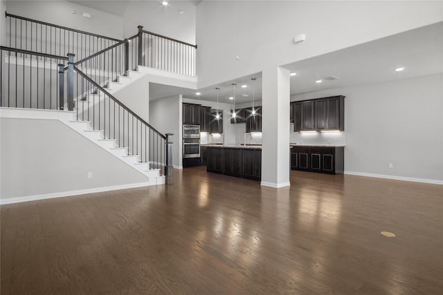 unfurnished living room with dark hardwood / wood-style flooring, sink, and a towering ceiling