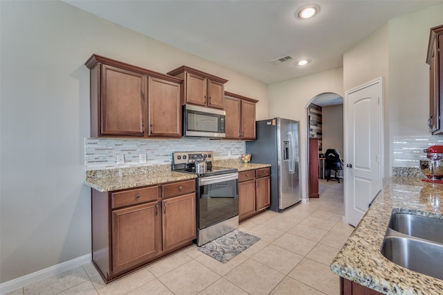 kitchen with stainless steel appliances, light stone counters, and backsplash