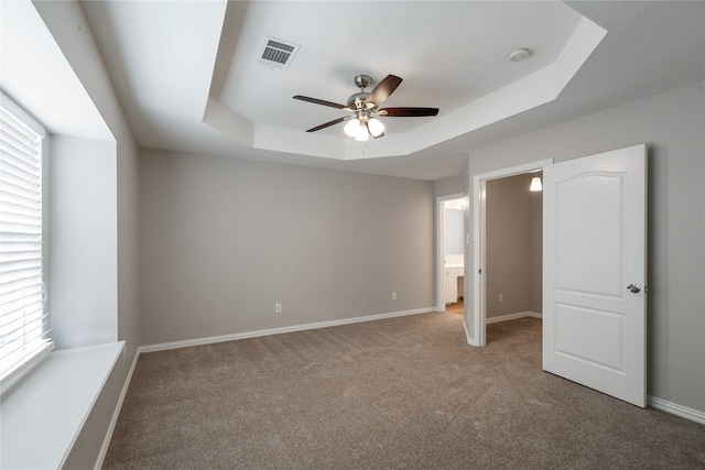 unfurnished bedroom with connected bathroom, ceiling fan, a raised ceiling, and multiple windows