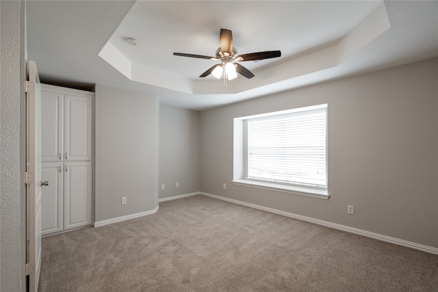 unfurnished bedroom with ceiling fan, light colored carpet, and a raised ceiling