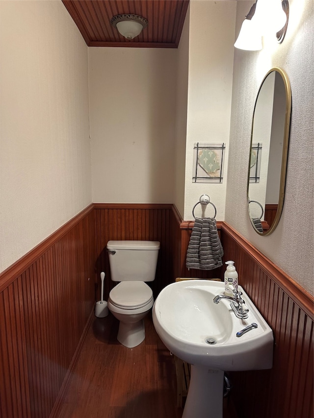 bathroom featuring hardwood / wood-style flooring, wood walls, toilet, and sink