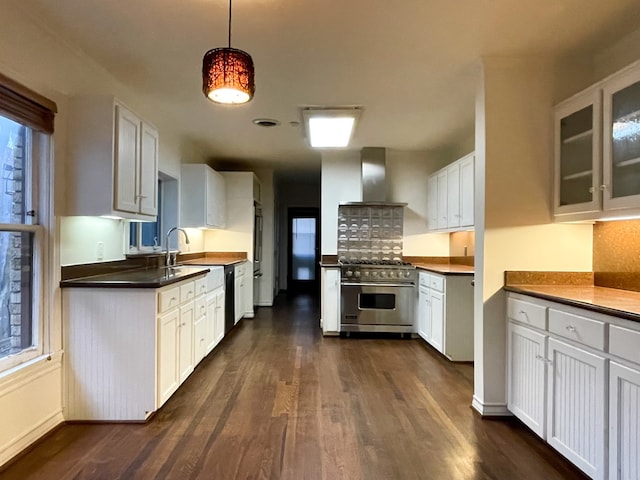 kitchen with pendant lighting, high end stainless steel range oven, dark wood-type flooring, white cabinets, and wall chimney exhaust hood