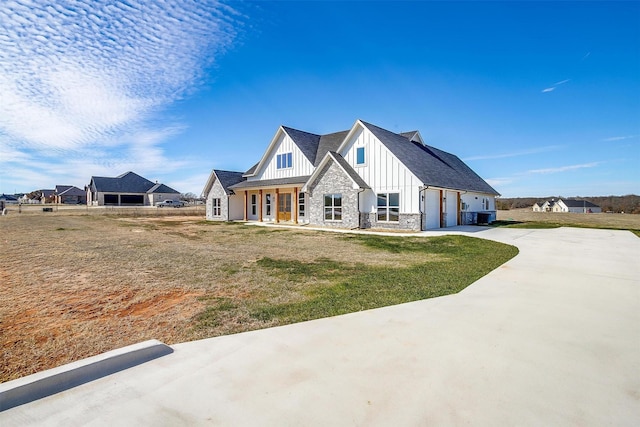 modern farmhouse with a porch, a garage, stone siding, driveway, and board and batten siding