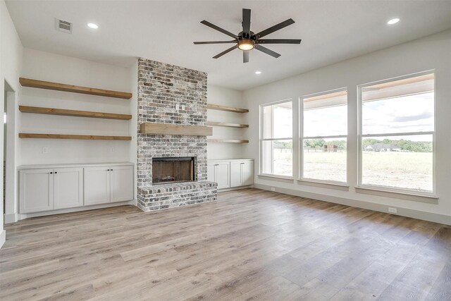 unfurnished living room featuring light wood-type flooring, ceiling fan, beamed ceiling, and a brick fireplace