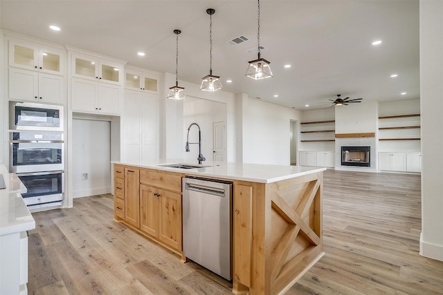 kitchen with a kitchen island with sink, ceiling fan, appliances with stainless steel finishes, a large fireplace, and white cabinetry