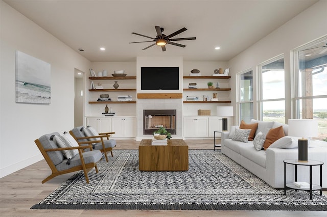 living room with a tiled fireplace, ceiling fan, and light hardwood / wood-style floors