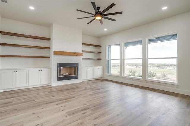 unfurnished living room featuring a tiled fireplace, ceiling fan, and light wood-type flooring