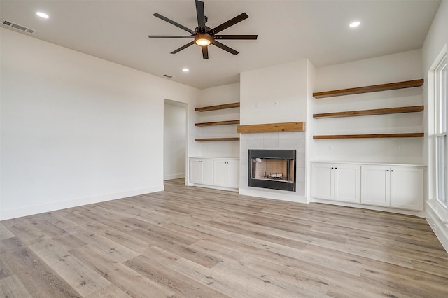 unfurnished living room featuring ceiling fan, a tiled fireplace, and light hardwood / wood-style flooring