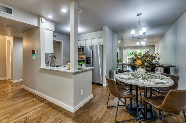 kitchen with appliances with stainless steel finishes, white cabinetry, sink, kitchen peninsula, and light wood-type flooring