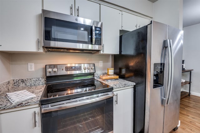 kitchen featuring stainless steel appliances, light stone counters, white cabinets, and light wood-type flooring