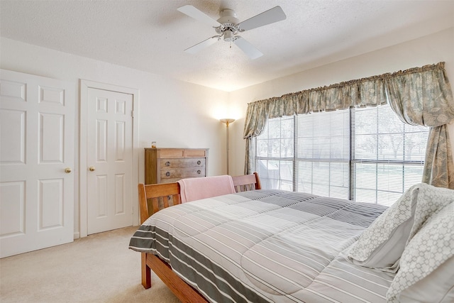 bedroom featuring a textured ceiling, light colored carpet, and ceiling fan