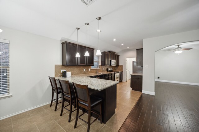 kitchen with appliances with stainless steel finishes, ceiling fan, decorative light fixtures, light hardwood / wood-style floors, and a breakfast bar area