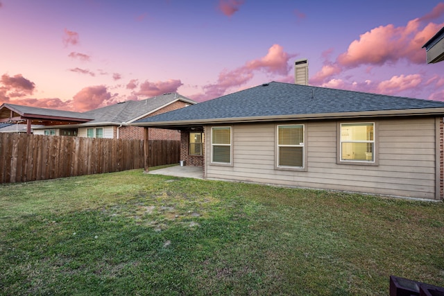 back house at dusk with a lawn and a patio area