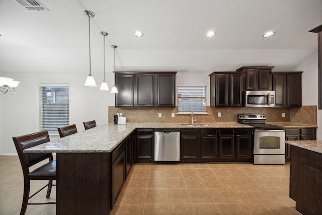 kitchen featuring kitchen peninsula, a kitchen breakfast bar, stainless steel appliances, sink, and decorative light fixtures