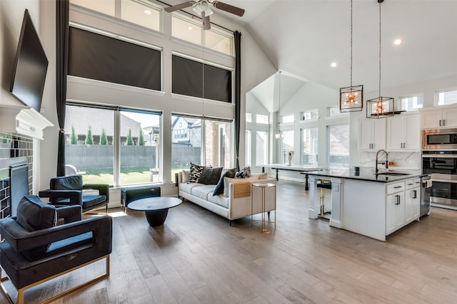 living room with light wood-type flooring, ceiling fan with notable chandelier, high vaulted ceiling, and sink