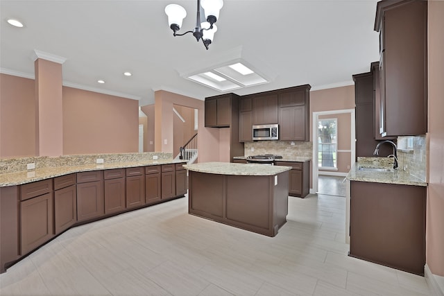 kitchen with appliances with stainless steel finishes, ornamental molding, a kitchen island, and a notable chandelier