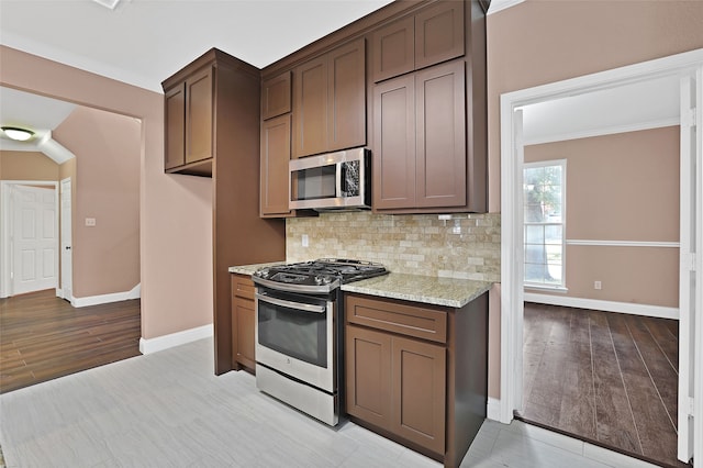 kitchen featuring light stone countertops, backsplash, light hardwood / wood-style floors, and appliances with stainless steel finishes