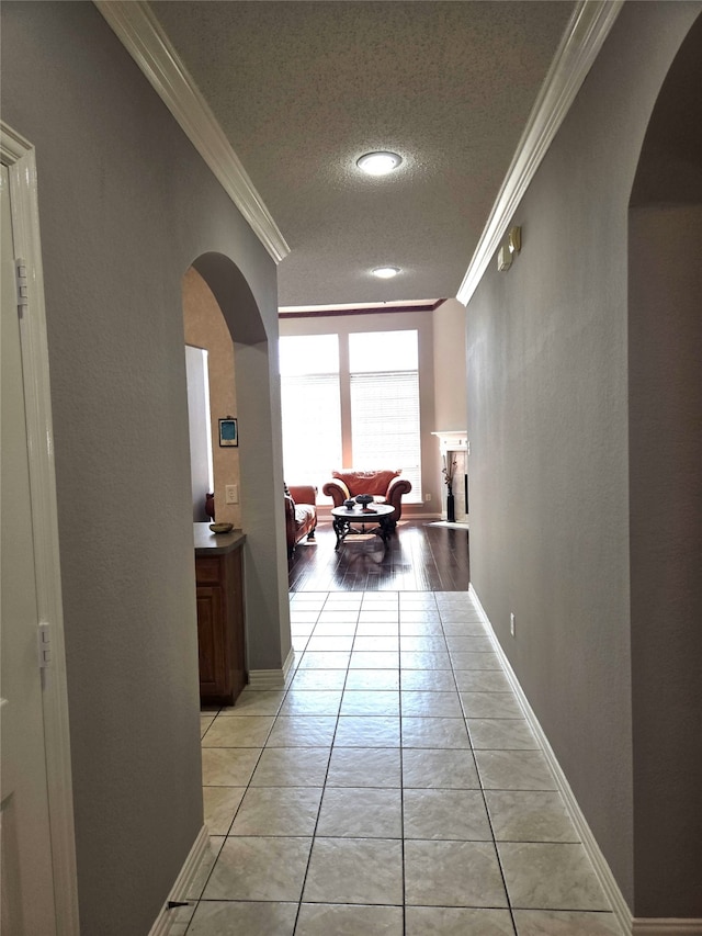 hall with ornamental molding, light wood-type flooring, and a textured ceiling