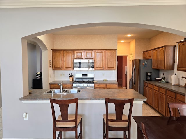 kitchen featuring light tile patterned flooring, sink, tasteful backsplash, appliances with stainless steel finishes, and a breakfast bar