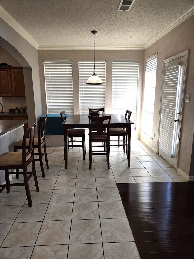 dining area with a textured ceiling, ornamental molding, and light hardwood / wood-style flooring