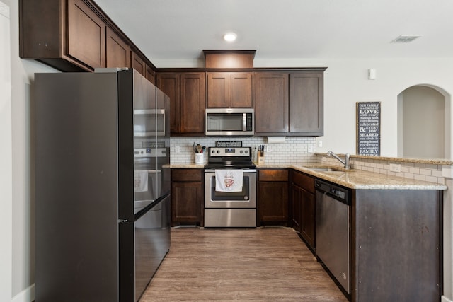 kitchen with light stone counters, stainless steel appliances, sink, and light hardwood / wood-style floors