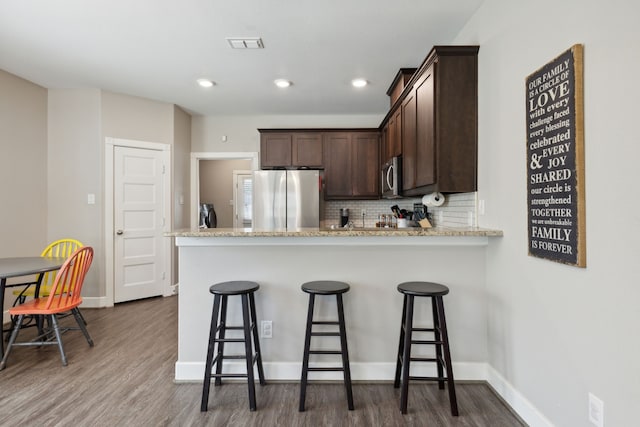 kitchen featuring light stone counters, hardwood / wood-style flooring, stainless steel appliances, and a breakfast bar