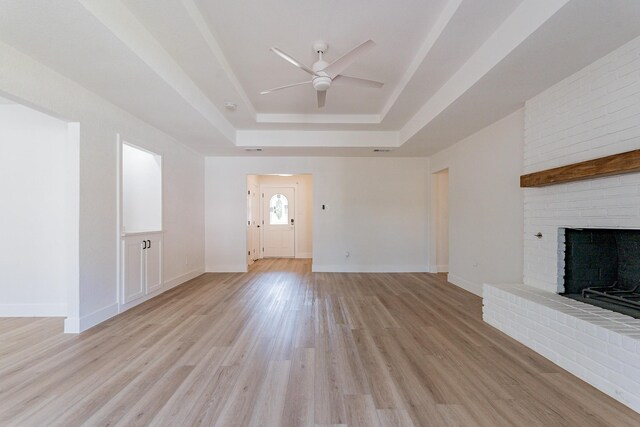 unfurnished living room with ceiling fan, a fireplace, light hardwood / wood-style floors, and a raised ceiling