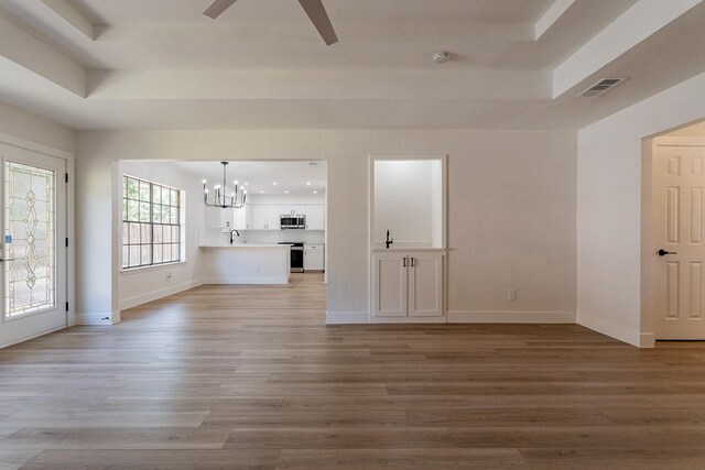 unfurnished living room featuring light hardwood / wood-style flooring, a healthy amount of sunlight, ceiling fan with notable chandelier, and a tray ceiling