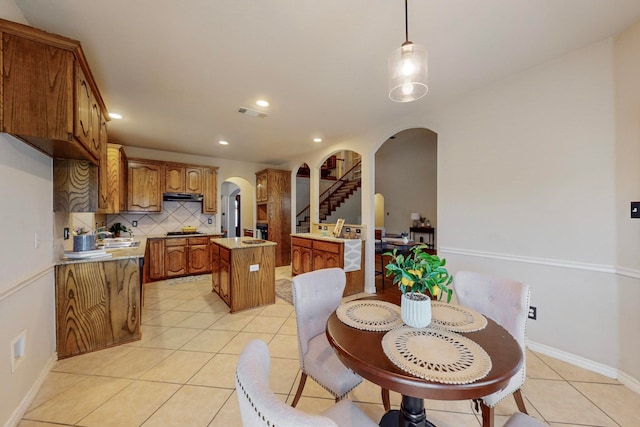 kitchen with light tile patterned floors, stainless steel gas stovetop, a center island, decorative backsplash, and hanging light fixtures