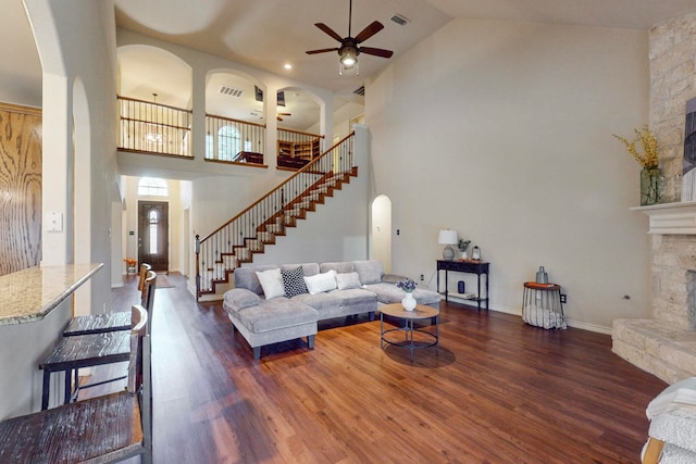 living room with ceiling fan, dark hardwood / wood-style floors, a stone fireplace, and high vaulted ceiling