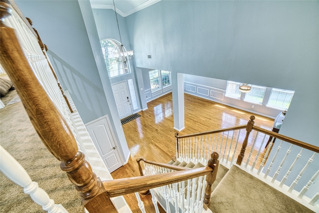 staircase featuring hardwood / wood-style floors, a towering ceiling, ornamental molding, and an inviting chandelier