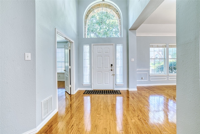 entryway featuring light hardwood / wood-style flooring, a towering ceiling, and ornamental molding