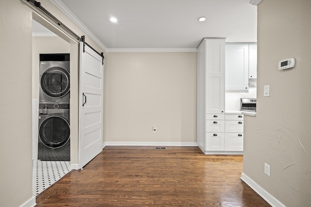 washroom featuring a barn door, dark wood-type flooring, crown molding, and stacked washer and clothes dryer