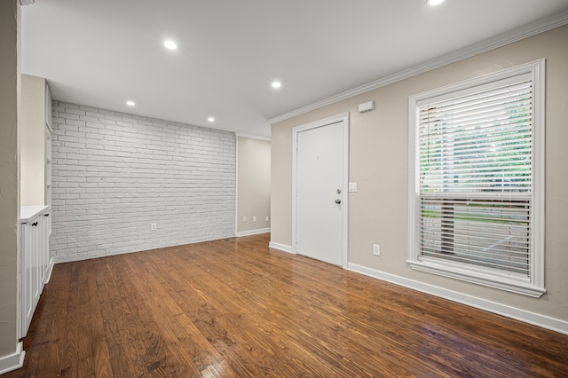 unfurnished room featuring hardwood / wood-style floors, ornamental molding, and brick wall