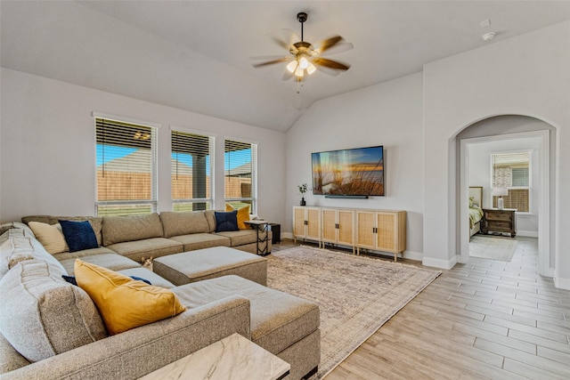 living area featuring baseboards, ceiling fan, light wood-type flooring, vaulted ceiling, and arched walkways