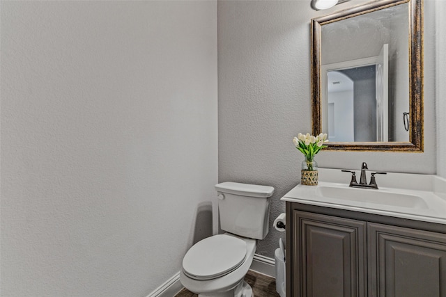 bathroom featuring vanity, wood finished floors, baseboards, toilet, and a textured wall