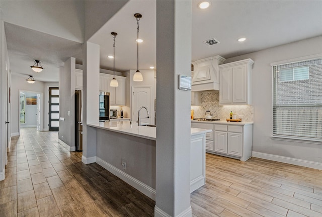 kitchen featuring decorative light fixtures, stainless steel gas stovetop, white cabinets, and light wood-type flooring