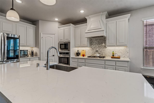 kitchen with pendant lighting, sink, premium range hood, white cabinetry, and stainless steel appliances